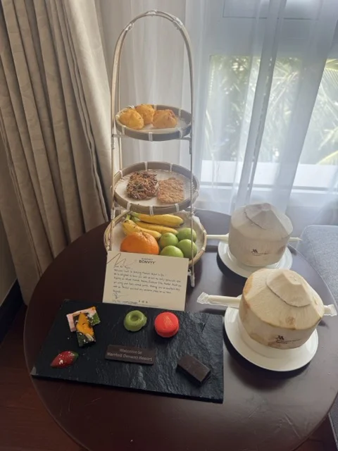 Marriott Bonvoy welcome amenity basket with tiered tray of pastries, tropical fruits, and coconuts — the kind of generic hotel personalization that misses what guests actually want